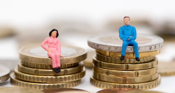 Die Figuren eines Mannes und einer Frau sitzen auf ungleichen Stapeln aus Geldmünzen. Foto: picture alliance | Andrea Warnecke. 
