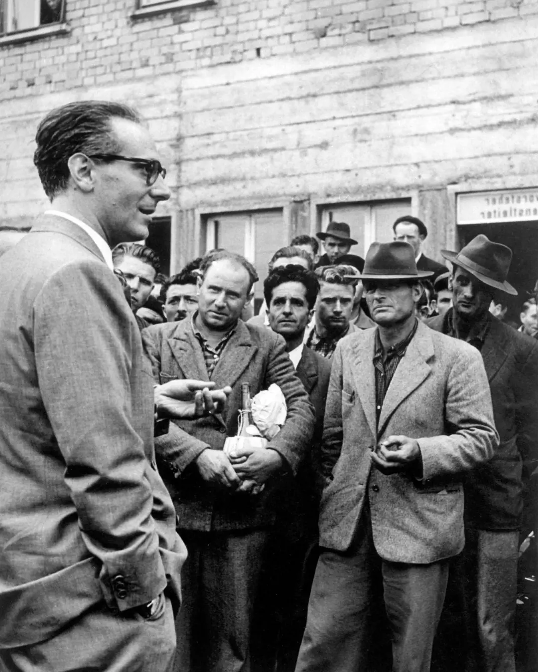 Hochkant schwarz-weiß Foto vom Konsul der gegenüber mehreren Männern steht. Die Männer sind im Gespräch.