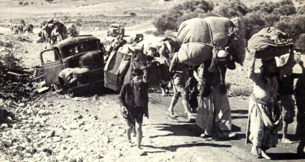Menschen gehen mit viel Gepäck eine Straße bergauf. Am Straßenrand ein offenbar kaputtes Auto.