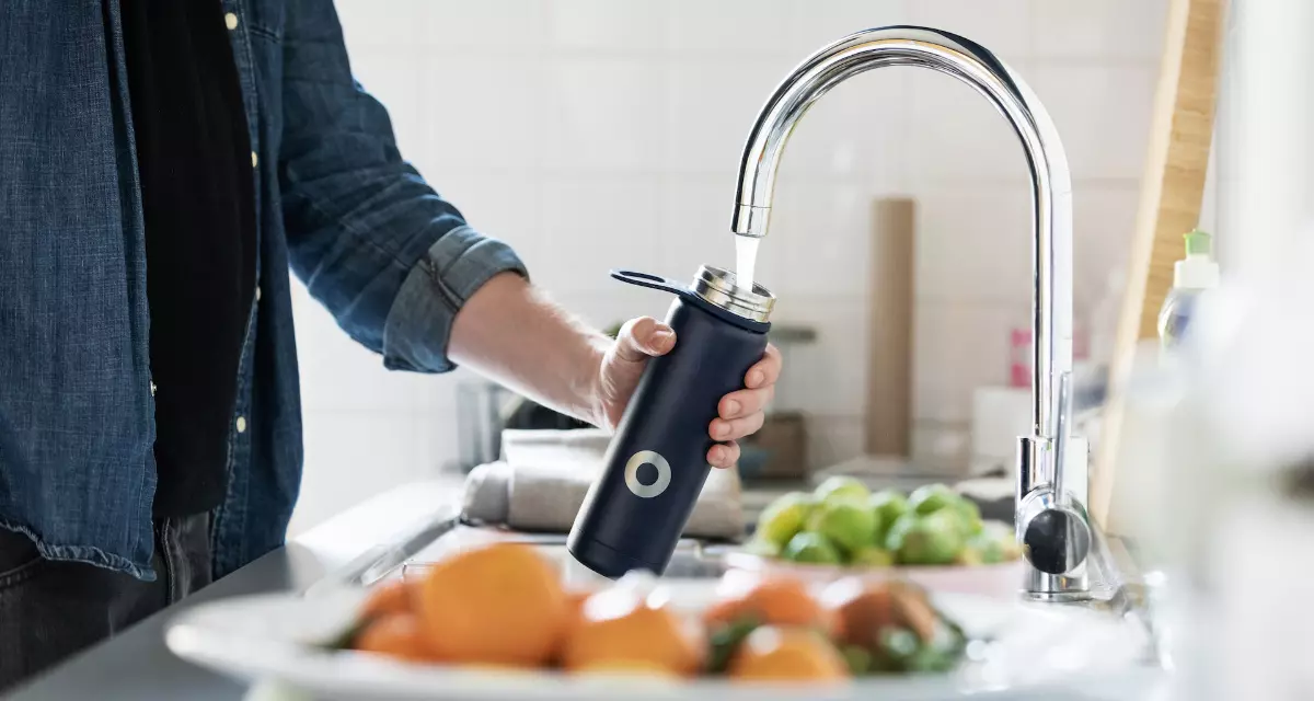 Mensch befüllt Flasche mit Leitungswasser.