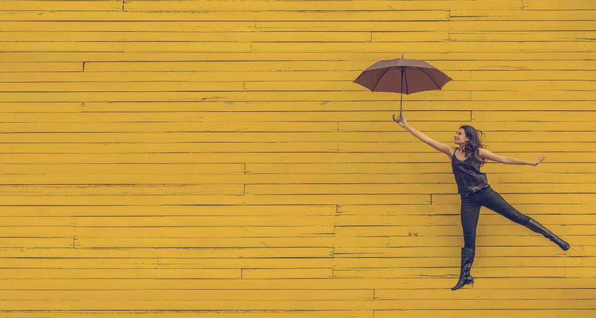 Mädchen mit Regenschirm vor gelber Wand.