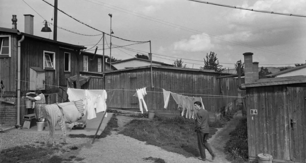 Schwarz-weiß Foto von Holzhäusern, Wäsche die auf Leinen über eine Wiese zwischen den Hütten gespannt ist.