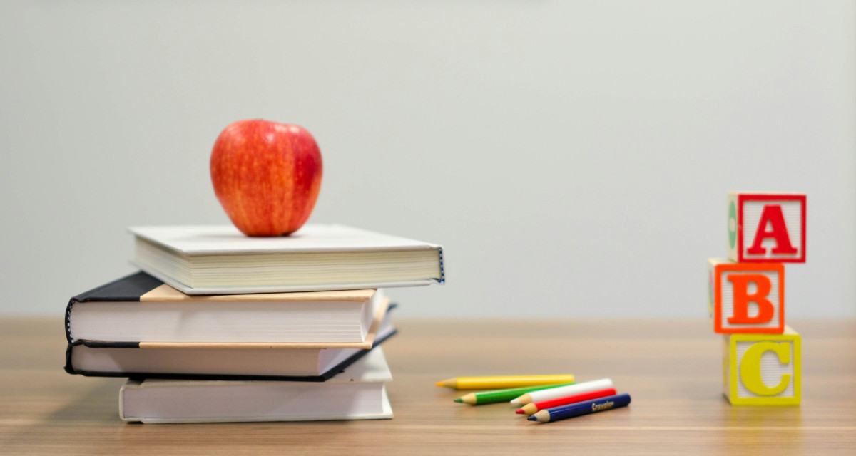 Bücher, Stifte und ein Apfel liegen auf einem Tisch, daneben die Buchstaben "A, B, C" als Bausteine.