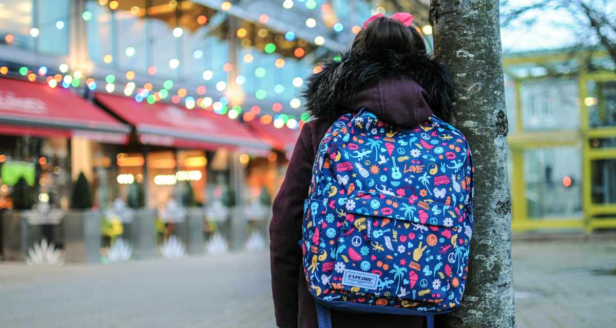 Ein Kind mit Schulranzen blickt auf ein Gebäude, an dem viele Lichter blinken.