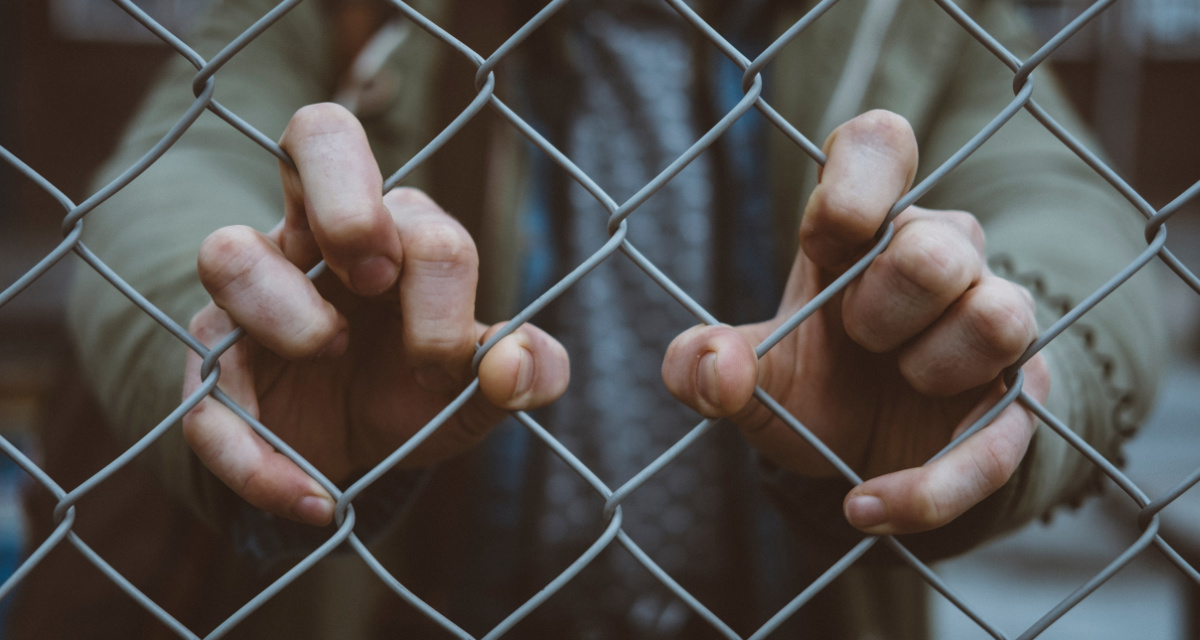 Hände greifen in einen Zaun. Foto: unsplash | Mitch Lensink