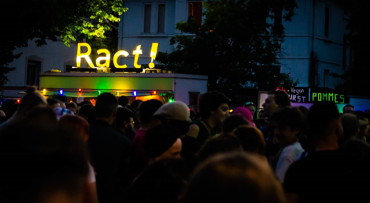 Titelbild Ract Infostand. Ract-Schriftzug als gelbes Neonschild in der Dämmerung.